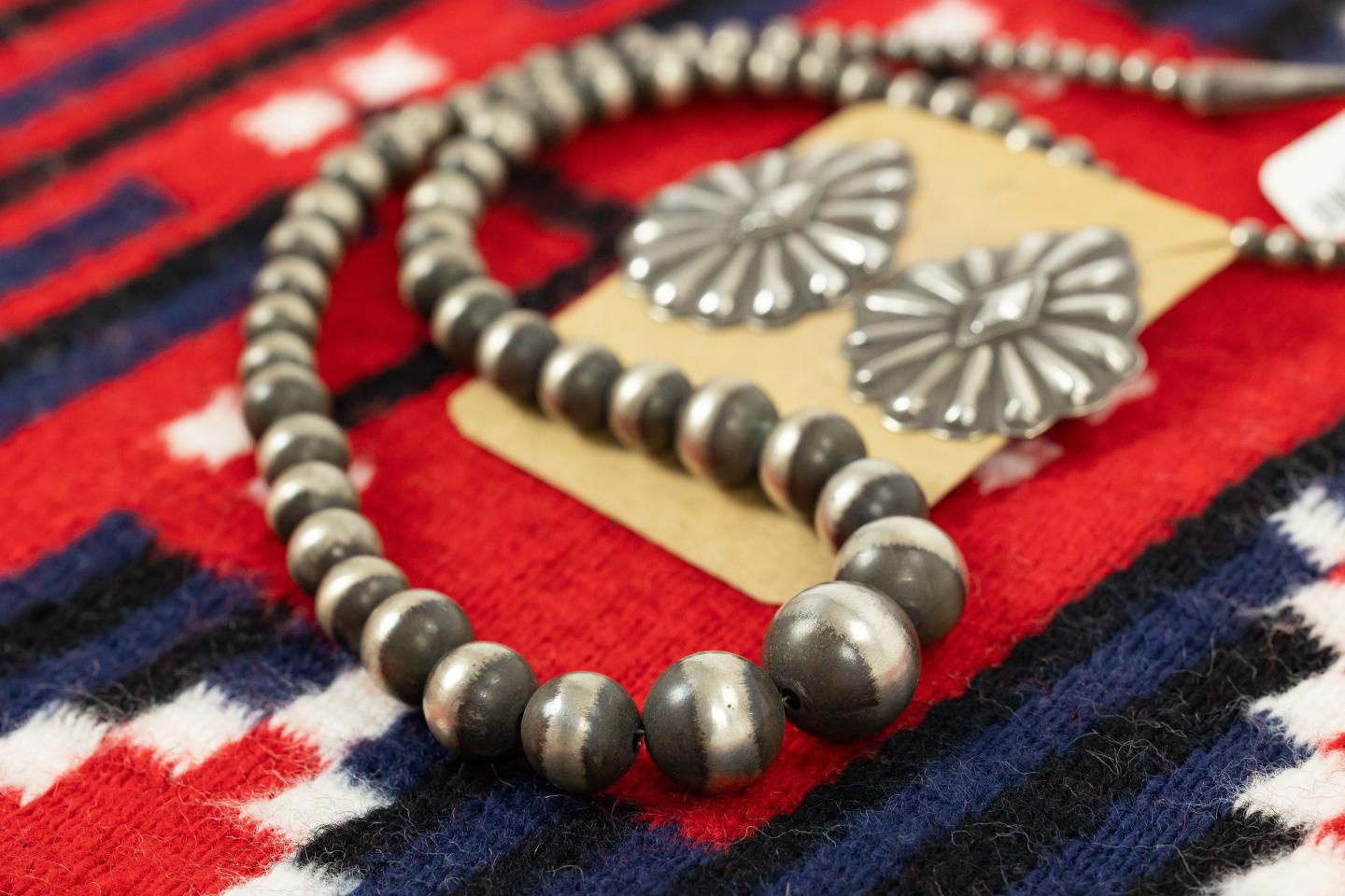Silver beaded necklace and earrings on red and blue patterned hand-woven Navajo rug.