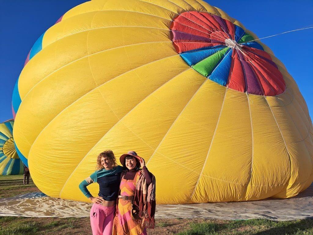 Two people smiling in front of a large yellow hot air balloon.