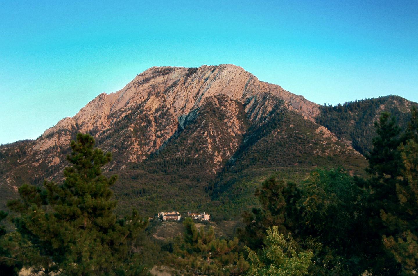 Rocky mountain under clear blue sky, surrounded by green trees.