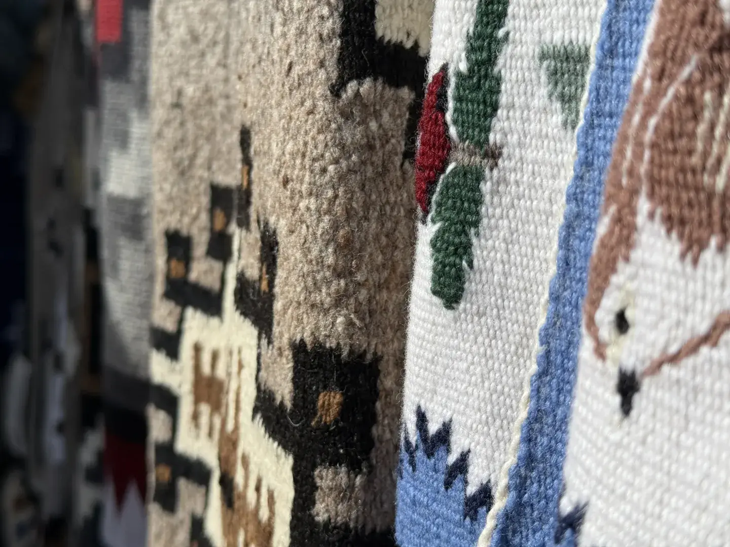 Woven Navajo rugs with colorful patterns hanging in a row.