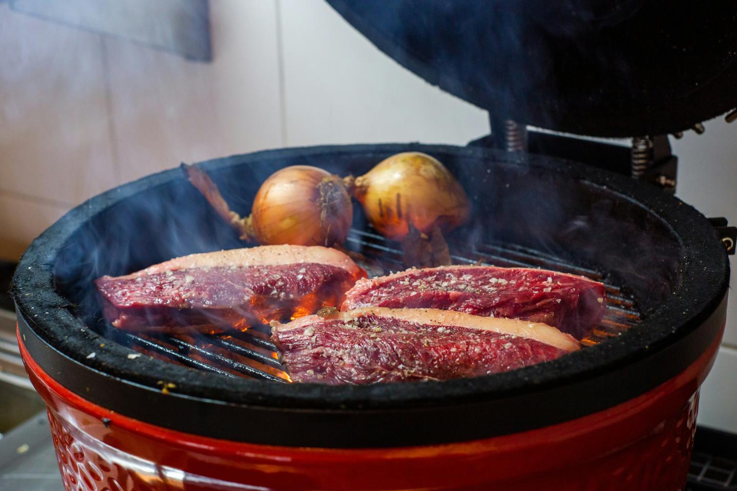 Steaks and onions grilling on a barbecue with smoke.