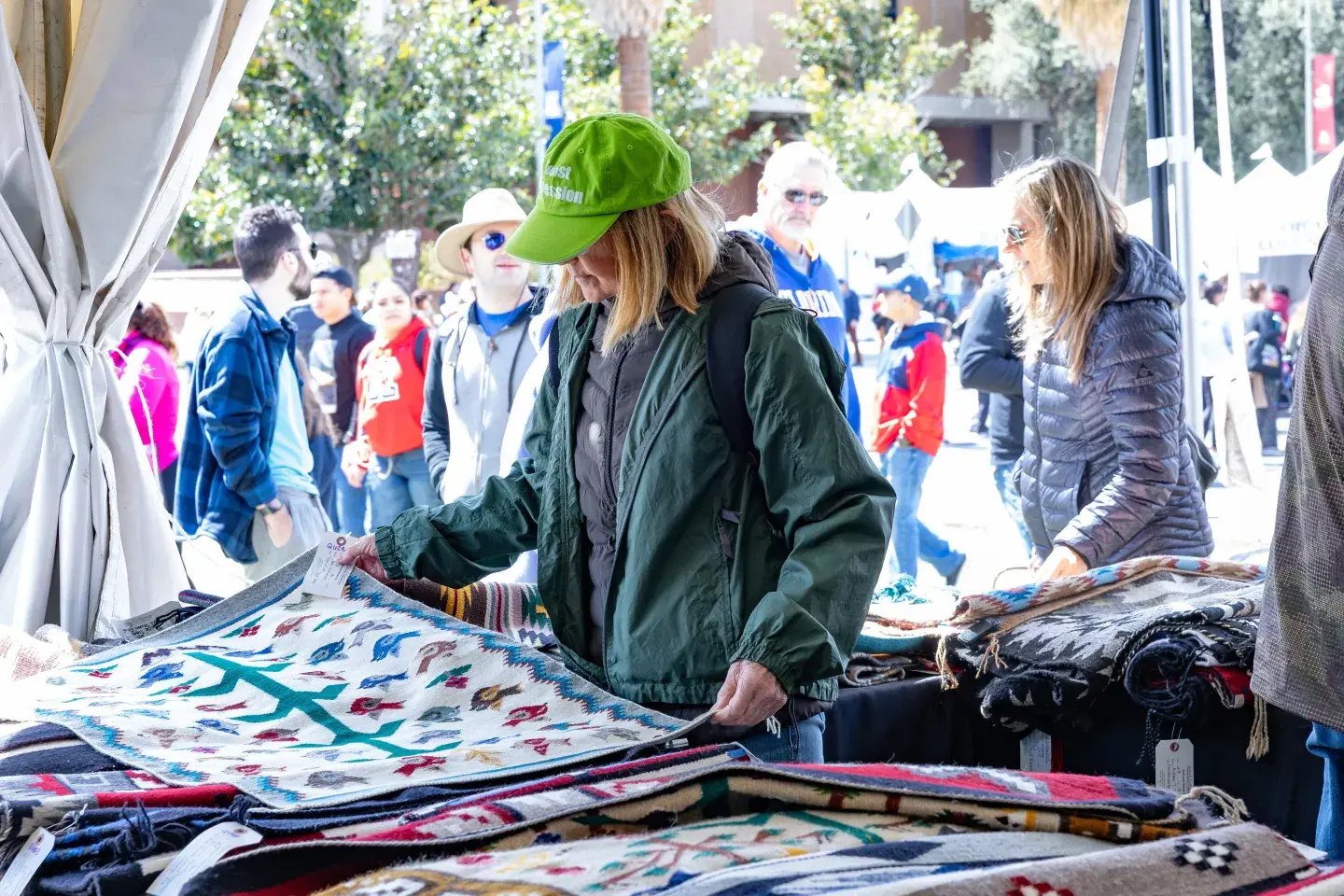 People browsing colorful Navajo weavings in daylight at Tucson Festival of Books.