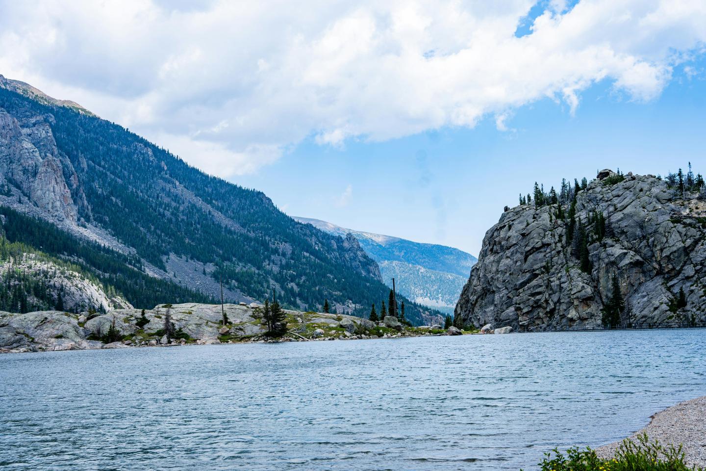 Mountain lake under a cloudy sky with rocky cliffs and trees.