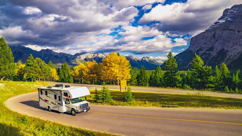 RV driving on a curved road through a scenic mountainous landscape with autumn trees.