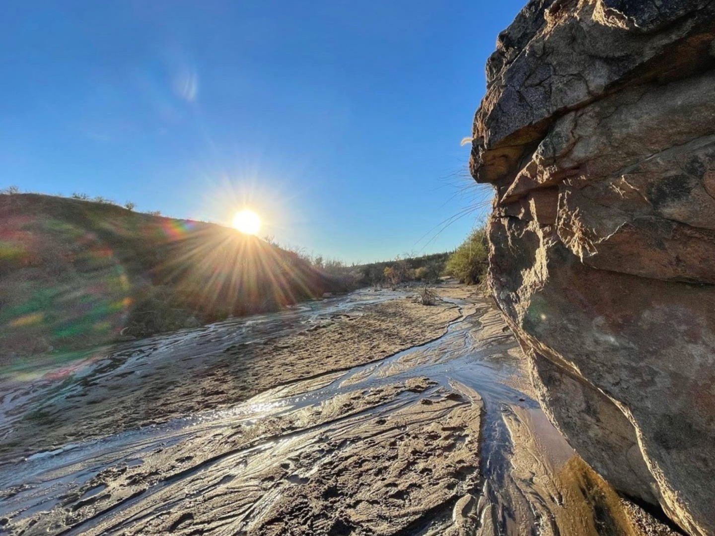 Sun setting over a rocky riverbed, casting warm light on the landscape.