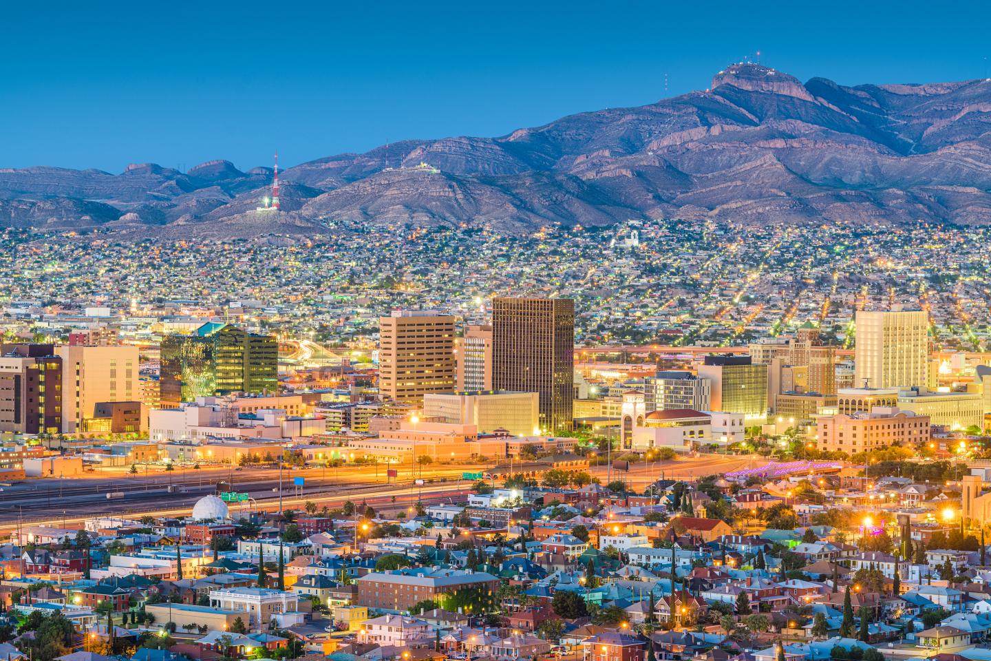 El Paso city skyline at dusk with mountains in the background, vibrant lights illuminating the scene.