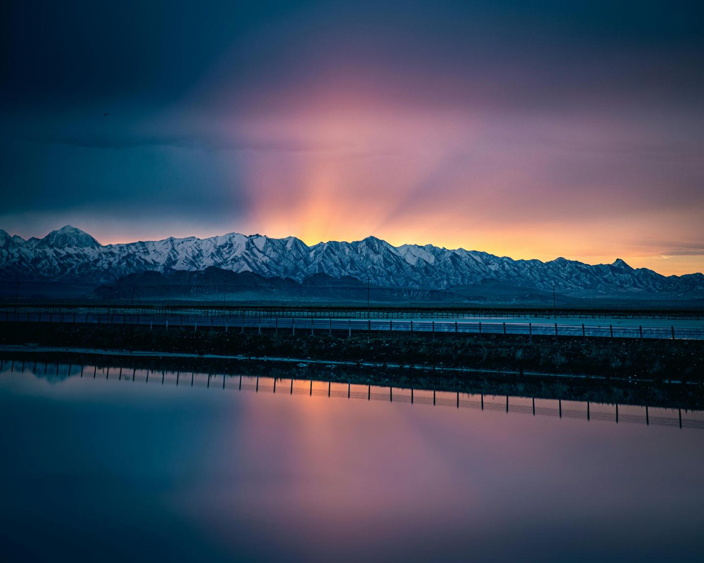 Sunset over snowy mountains, reflected in serene water.