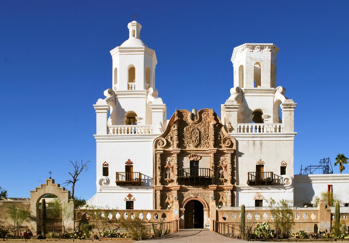 Historic white mission church with two towers against a clear blue sky.