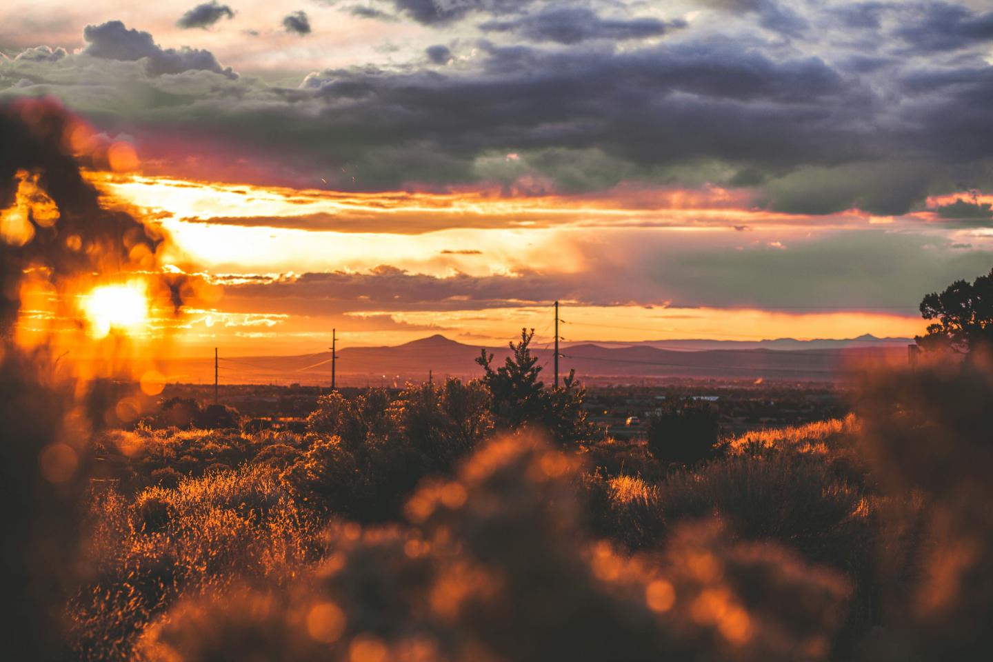 Sunset over a landscape with clouds and silhouettes of distant mountains and trees.