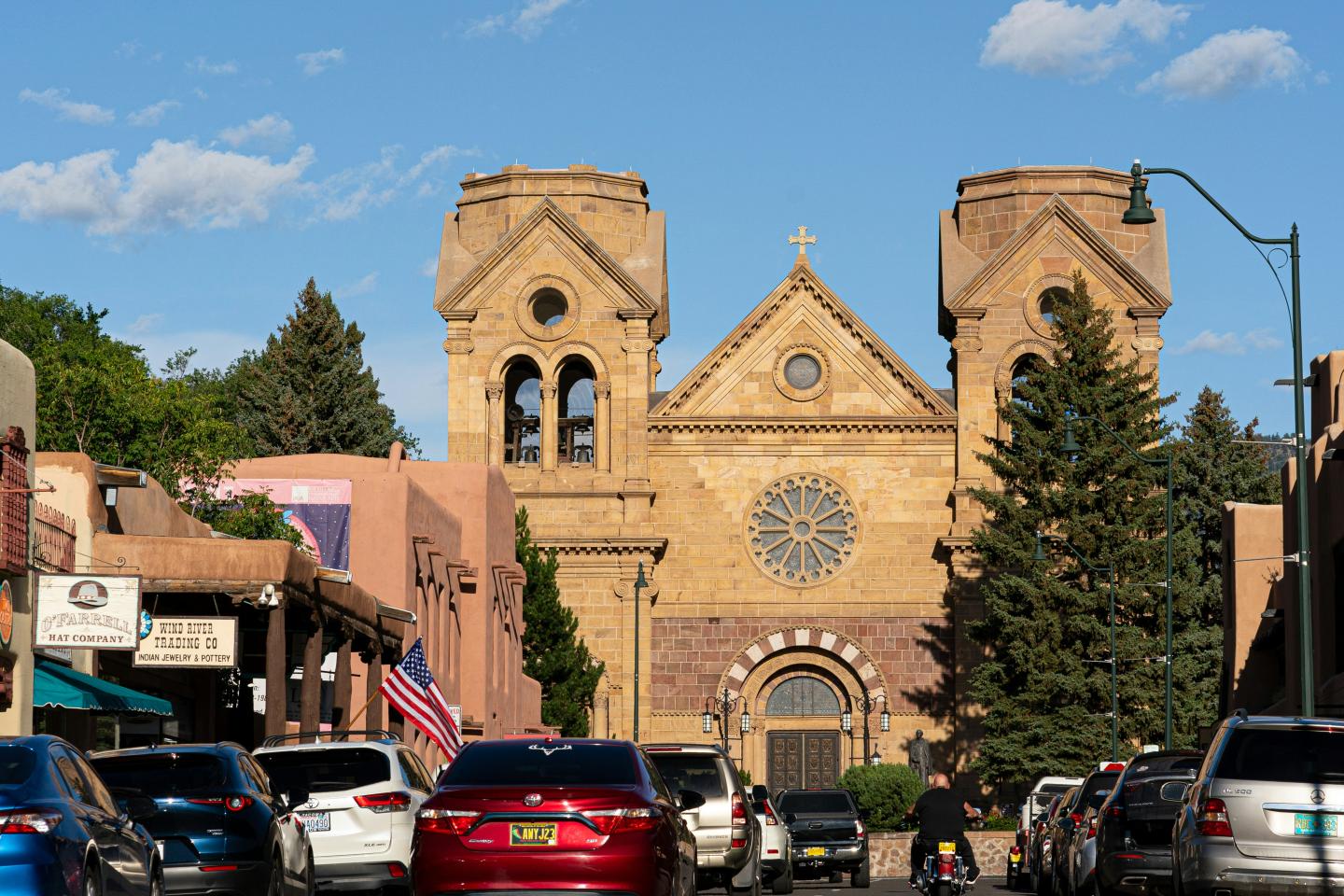 Historic cathedral with two towers, parked cars, and blue sky.