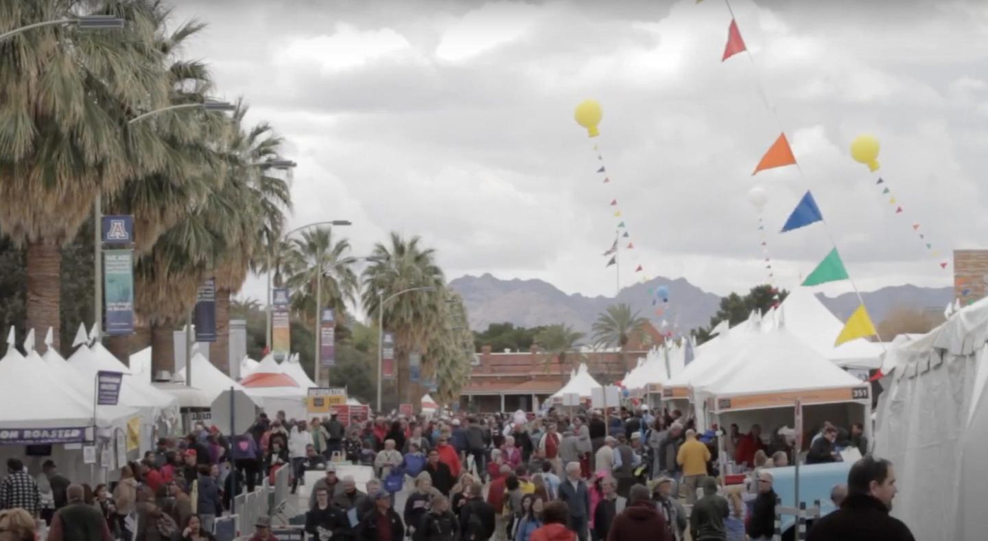 Crowded outdoor festival with white tents and colorful flags.