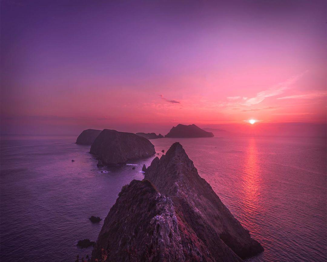 A purple sunset over rocky islands in the ocean.