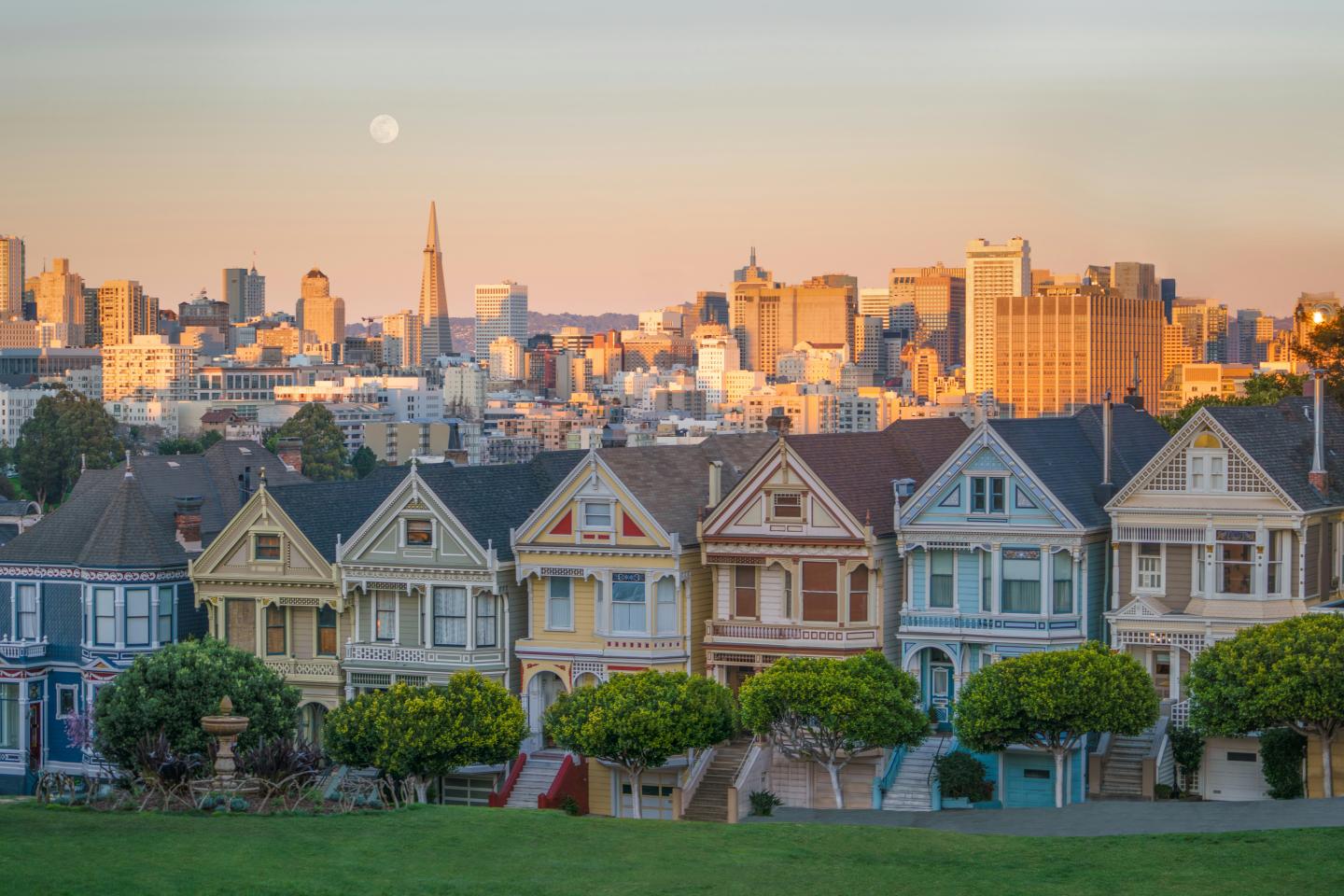 Colorful San Francisco houses in front of a city skyline at sunset.