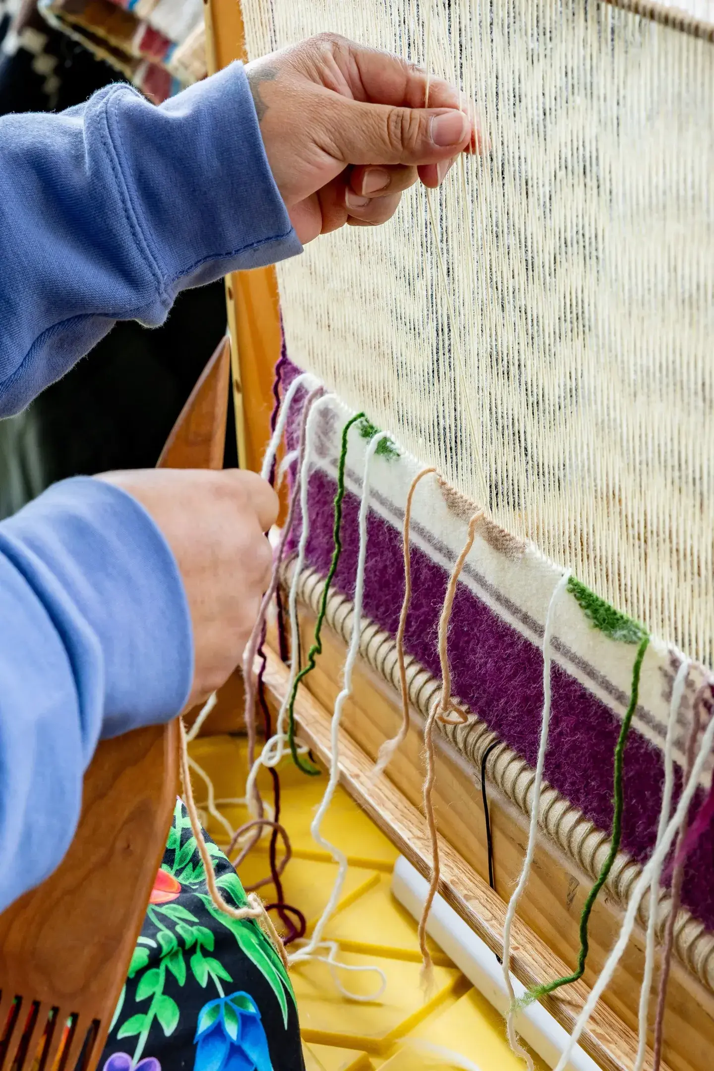 Hands weaving a colorful textile on a loom.