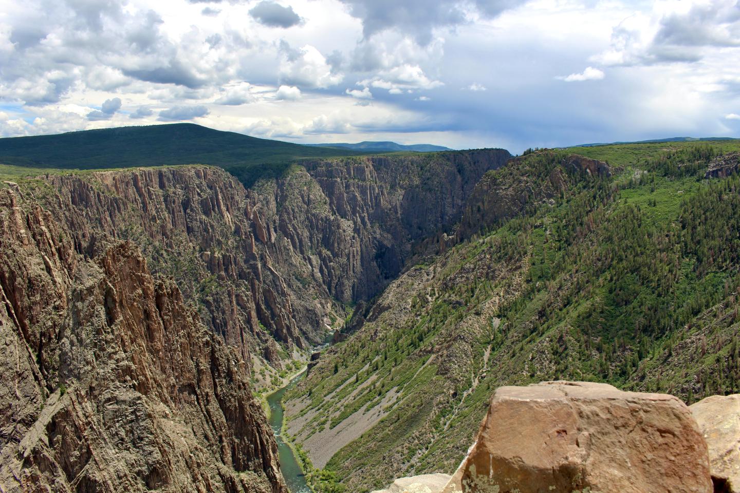 Rocky canyon with green slopes under a cloudy sky.