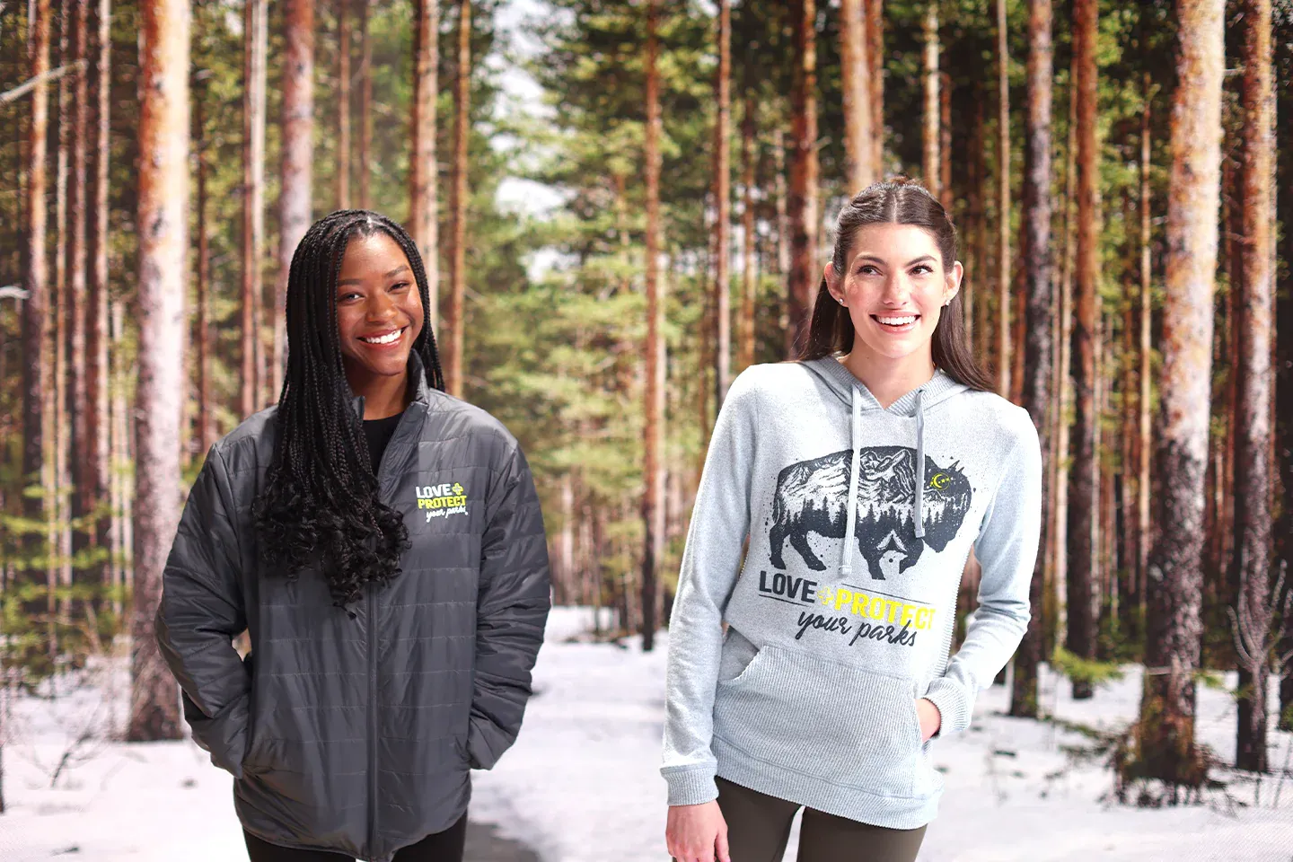 Two women smiling in a snowy forest, wearing casual outdoor clothing.