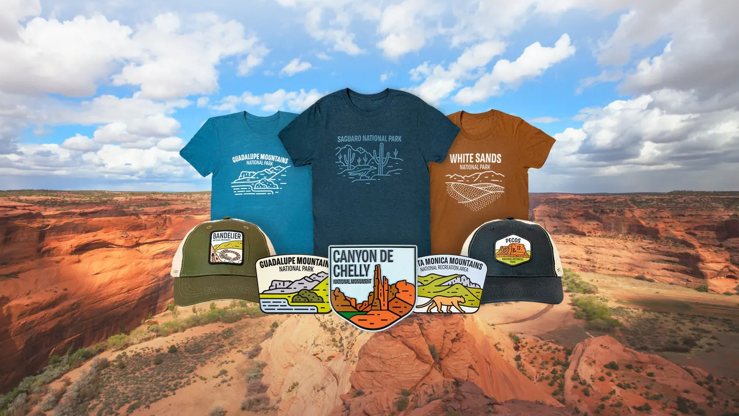 T-shirts and caps with scenic prints over a desert canyon backdrop.
