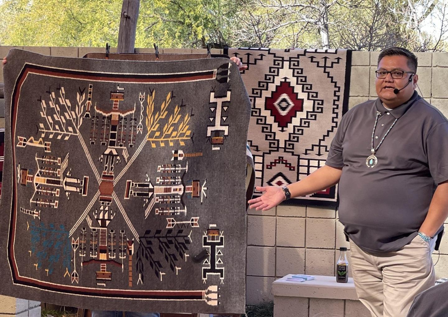 Wallace James Jr presenting intricate woven Navajo weavings outdoors.