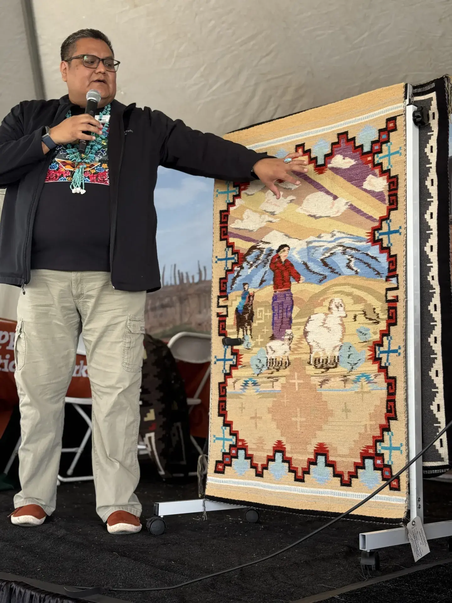 Wallace James Jr presenting colorful woven Navajo rug on stage at Tucson Festival of Books.
