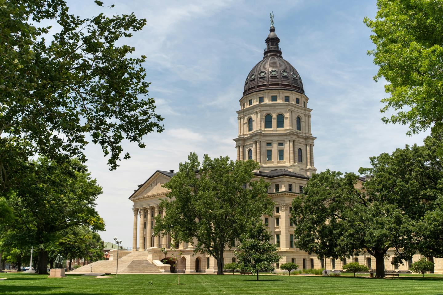 Historic capitol building with a dome, surrounded by trees and a blue sky.