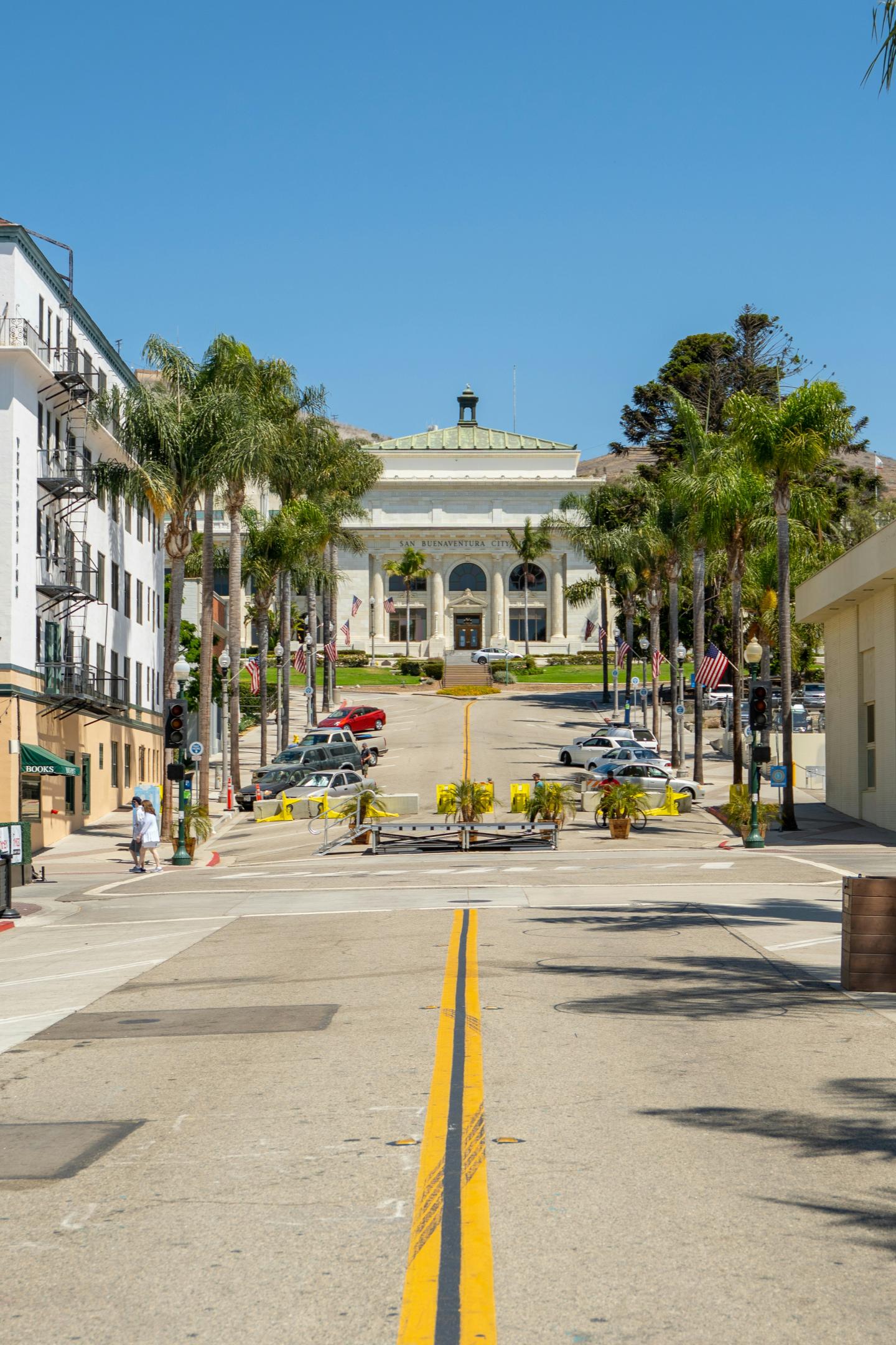 Street with palm trees leading to a white building under a clear blue sky.