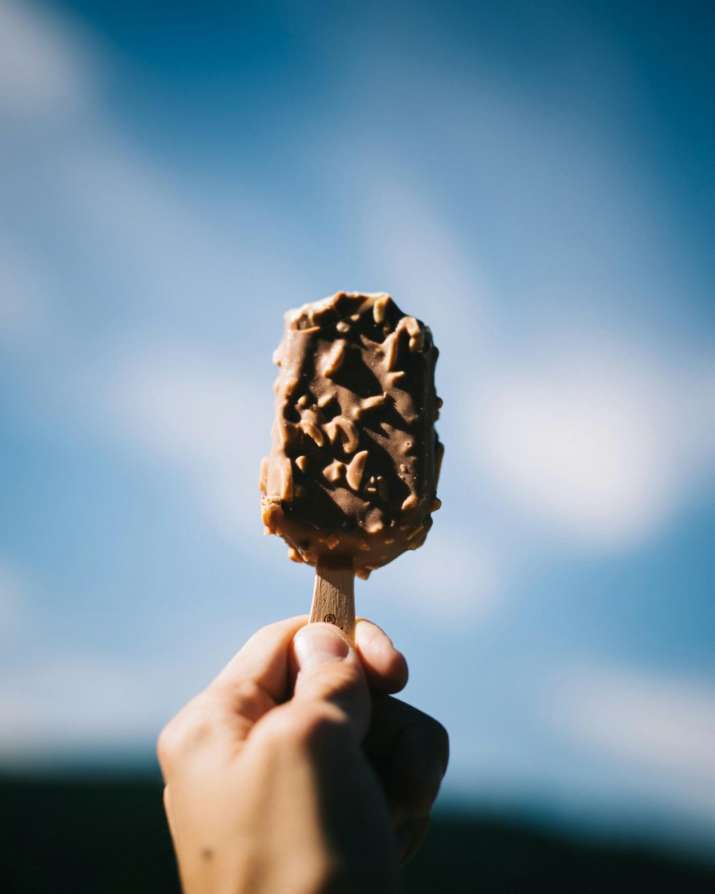 Chocolate ice cream bar held against a blue sky backdrop.