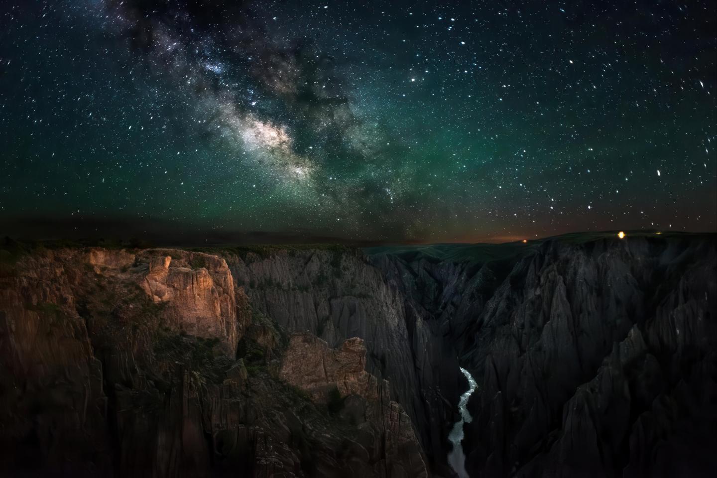 Starry sky over a canyon with a winding river at night.