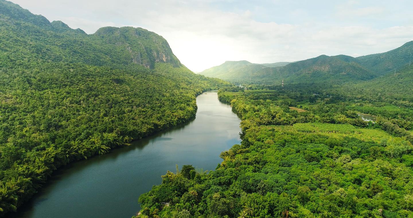 Lush green valley with a winding river and distant hills under a bright sky.