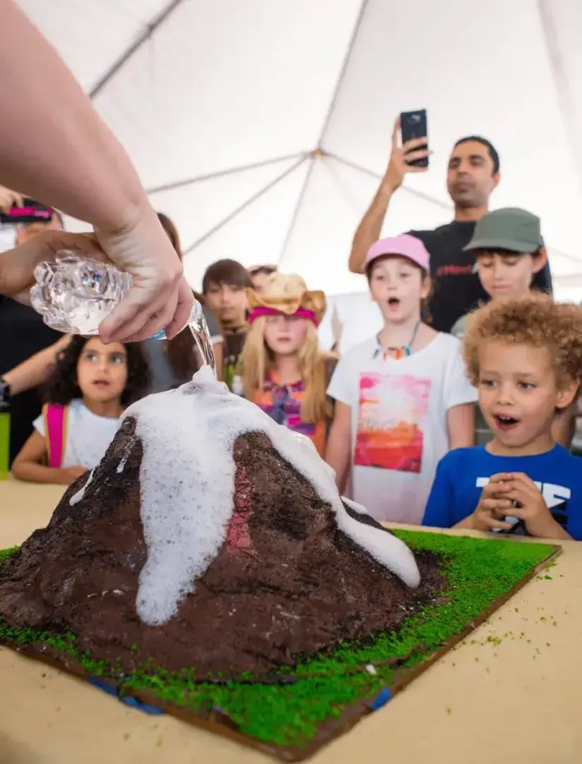 Children watch in awe as a baking soda volcano erupts.