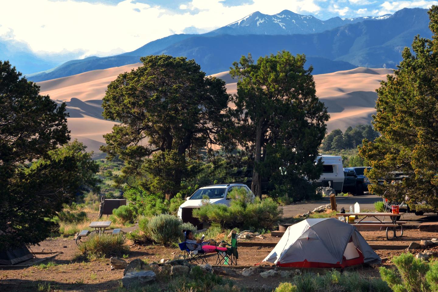 Camping site with a tent, trees, and mountains in the background.