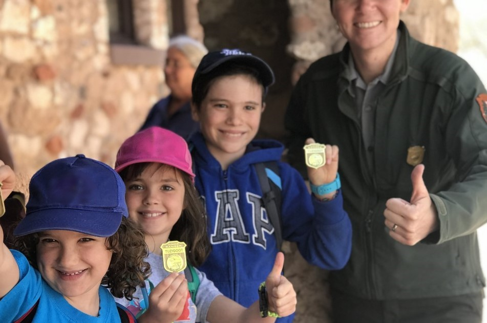 Three children and a ranger smile, holding Junior Ranger badges.