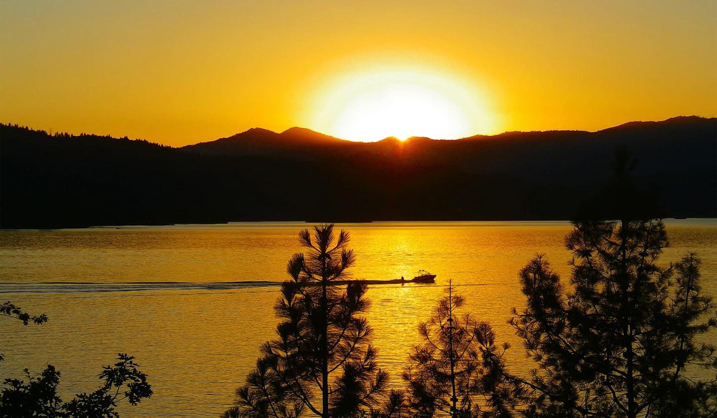 Golden sunset over a lake with silhouetted trees and hills.