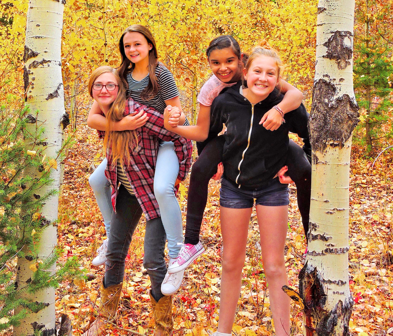 Four girls playing piggyback in an autumn forest.