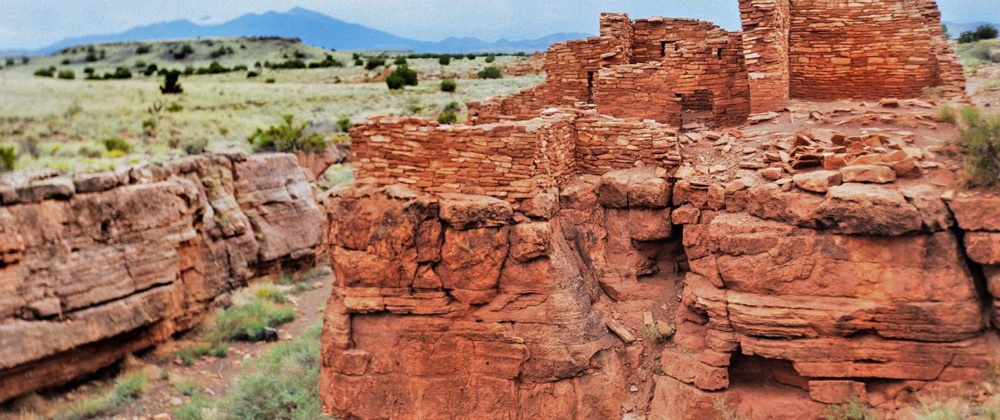 Red rock ruins with a mountainous landscape in the background.