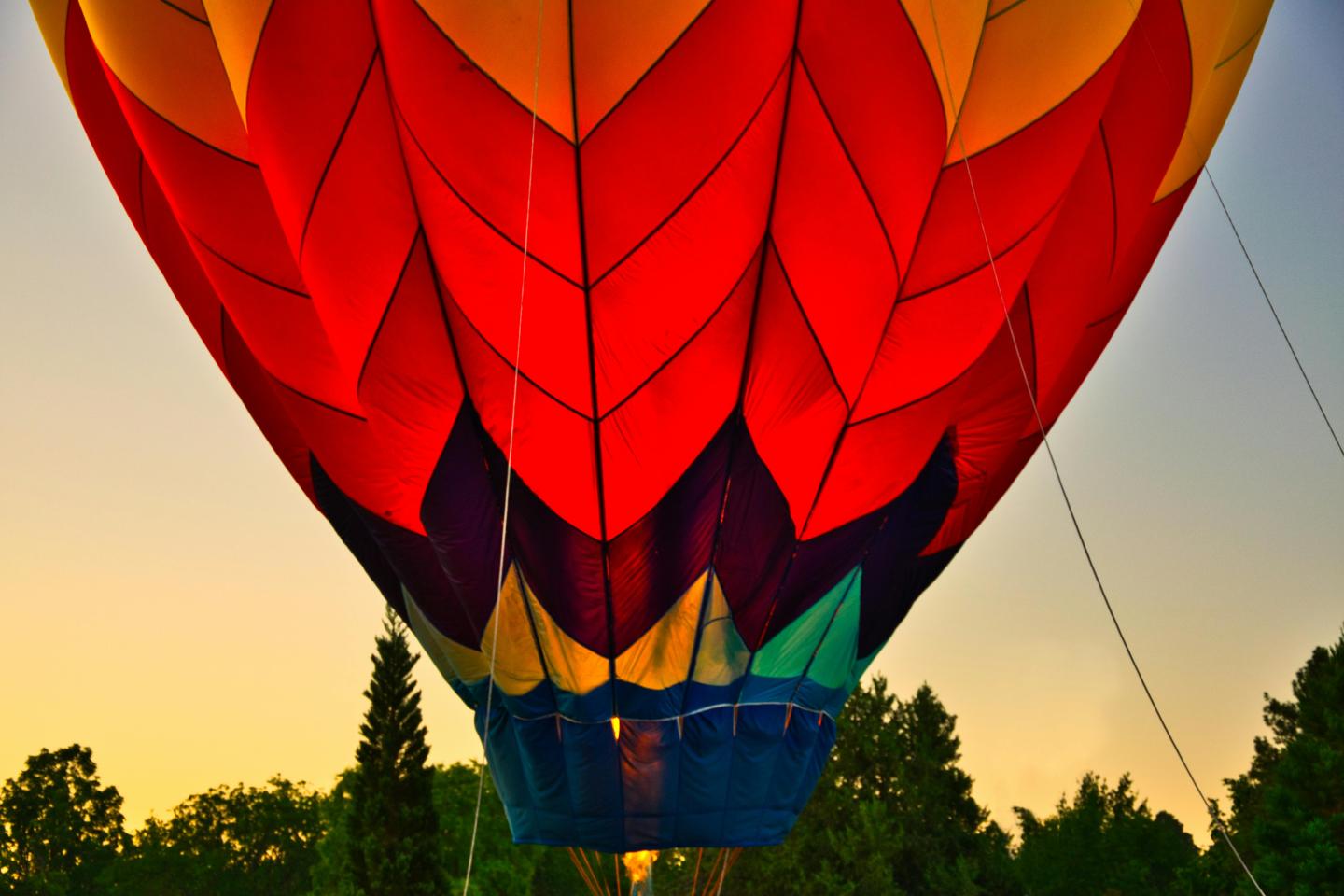 Colorful hot air balloon close-up with trees and sky at sunset.