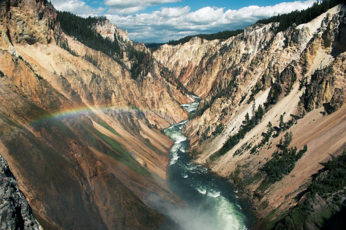 Steep canyon with river and rainbow under a blue sky.