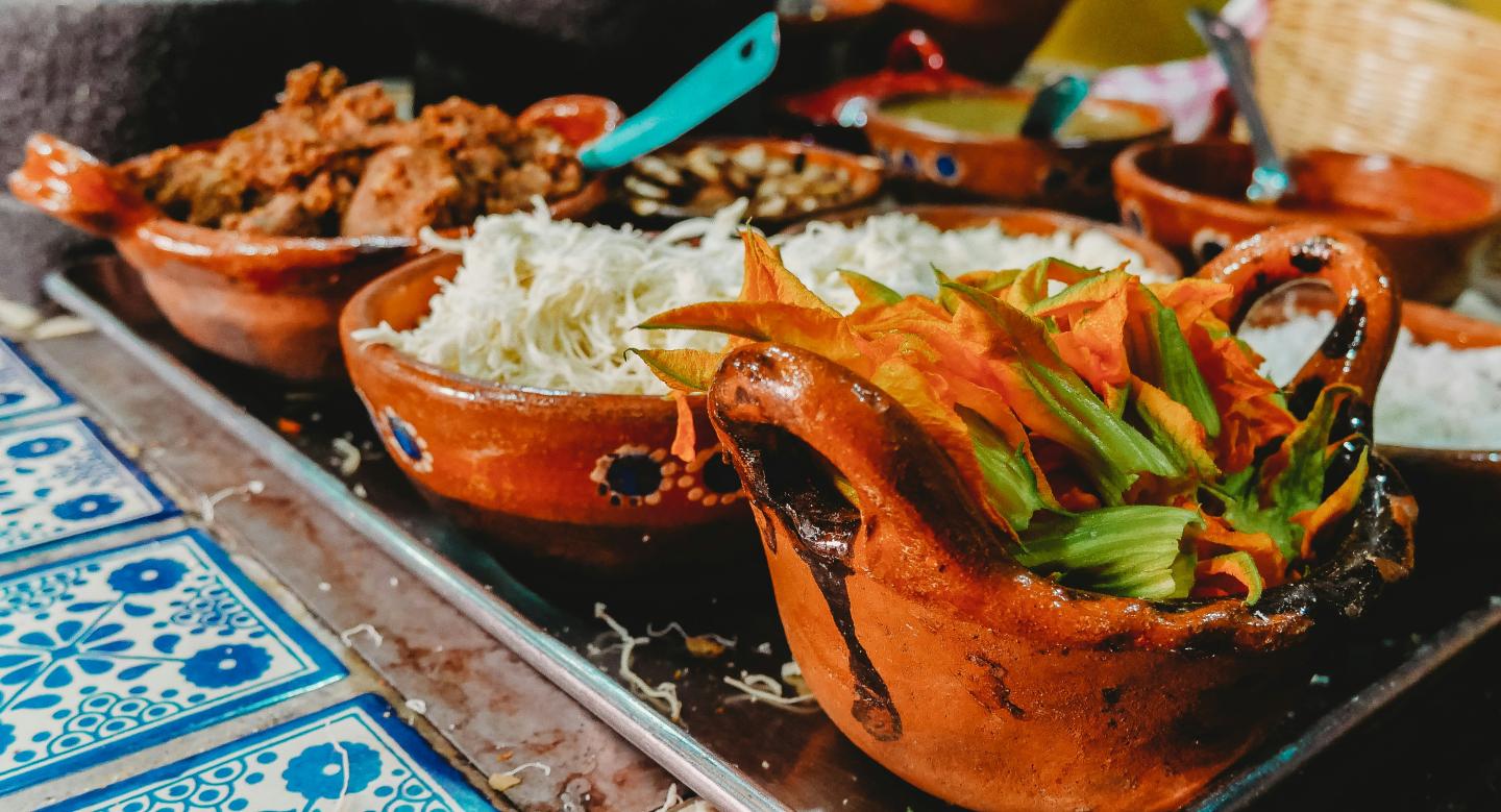Clay dishes with colorful vegetables and rice on a decorative table.