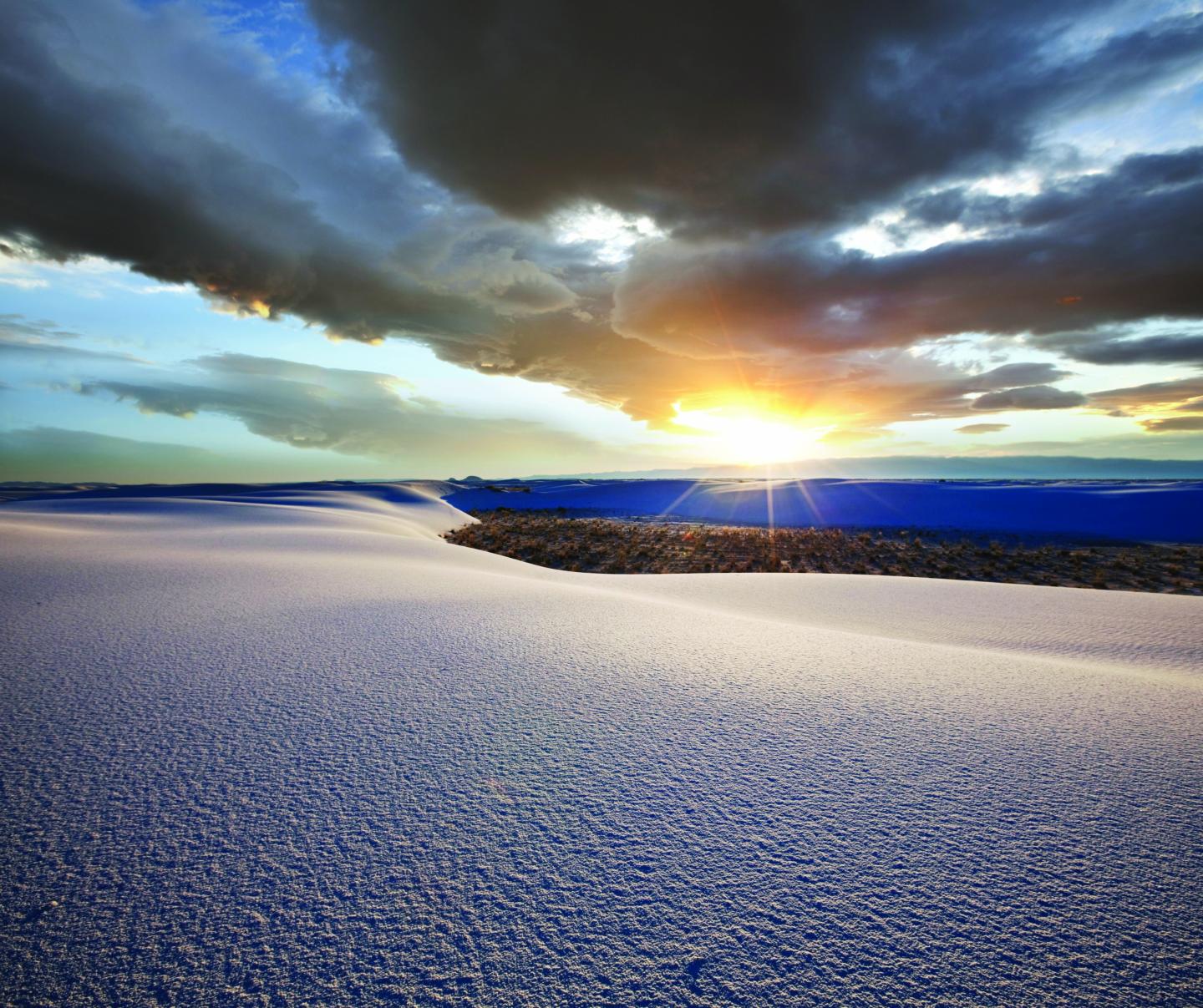 Snowy landscape with sunset and dramatic clouds.