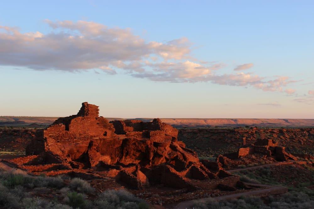 Ancient red rock ruins under a blue sky with scattered clouds.