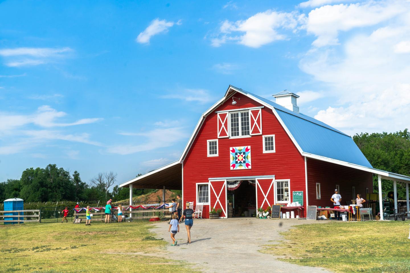 Red barn with blue roof under a bright sky, people walking in front.