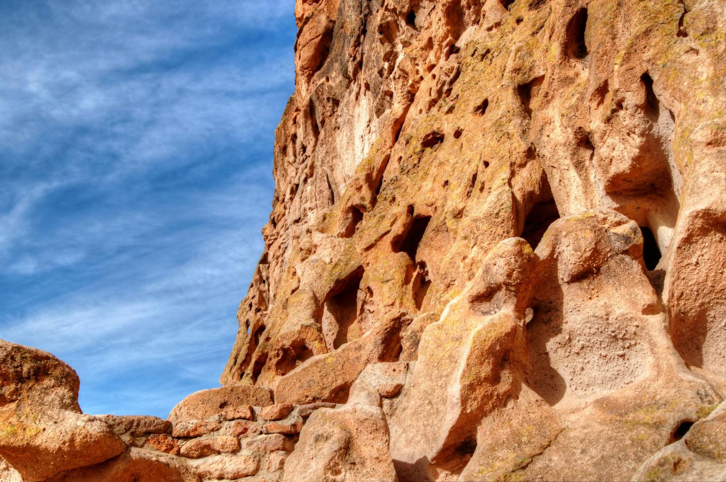 Rocky cliff against a blue sky with scattered clouds.