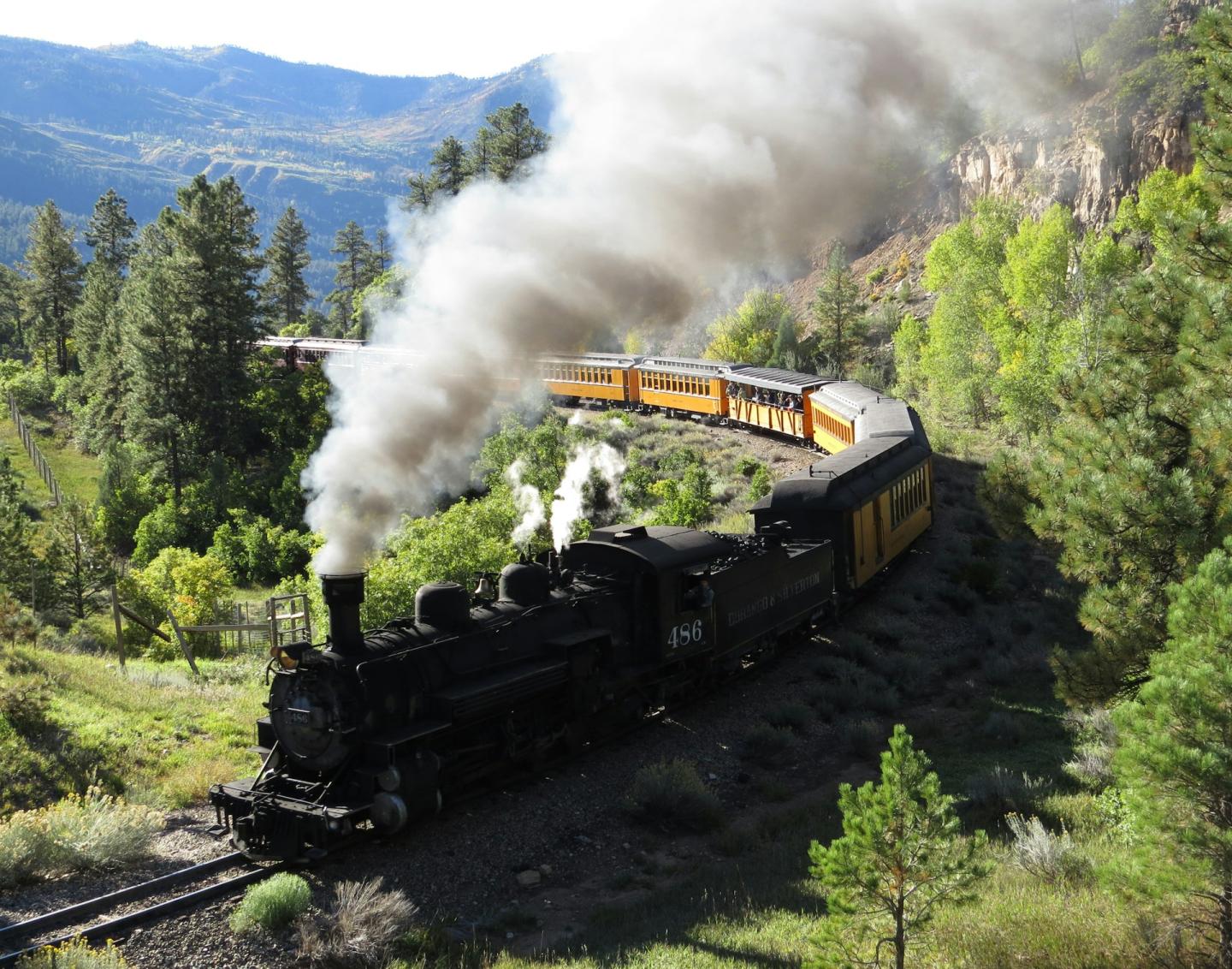 Steam train winding through forested mountains.