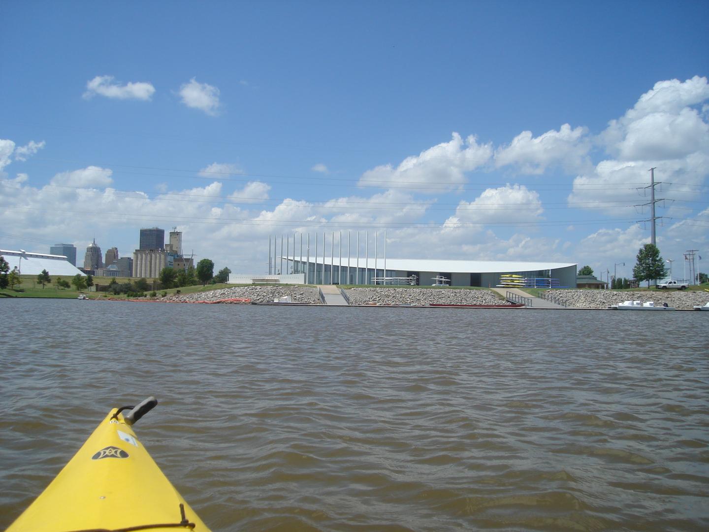 Yellow kayak on a river, cityscape and cloudy sky in the background.