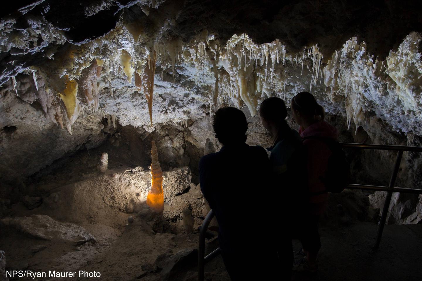 Tourists viewing illuminated cave formations in dim lighting.