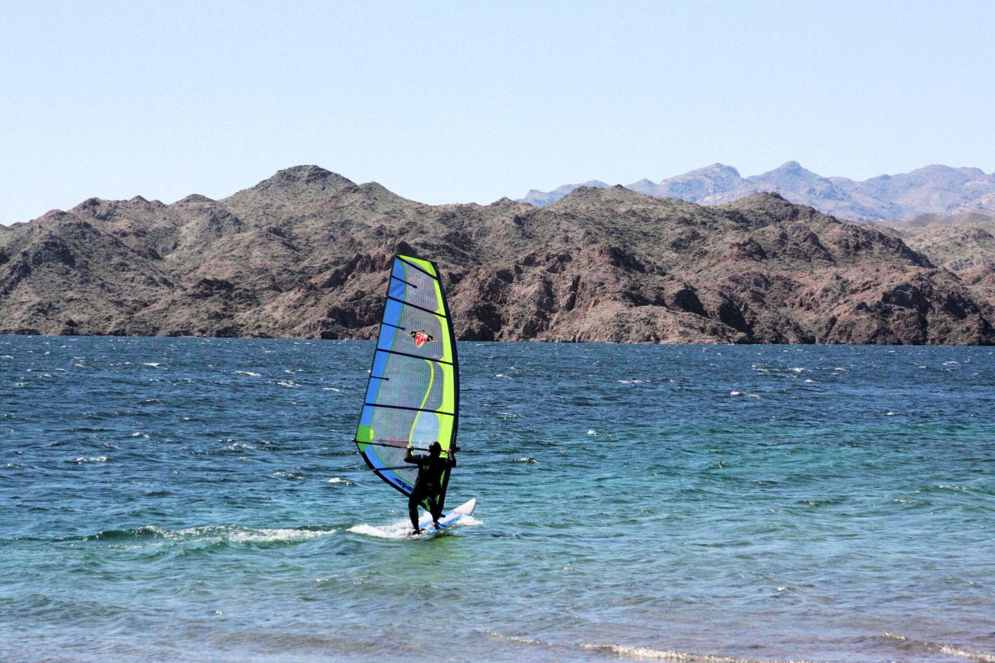 Windsurfer gliding on blue ocean near rocky mountains.