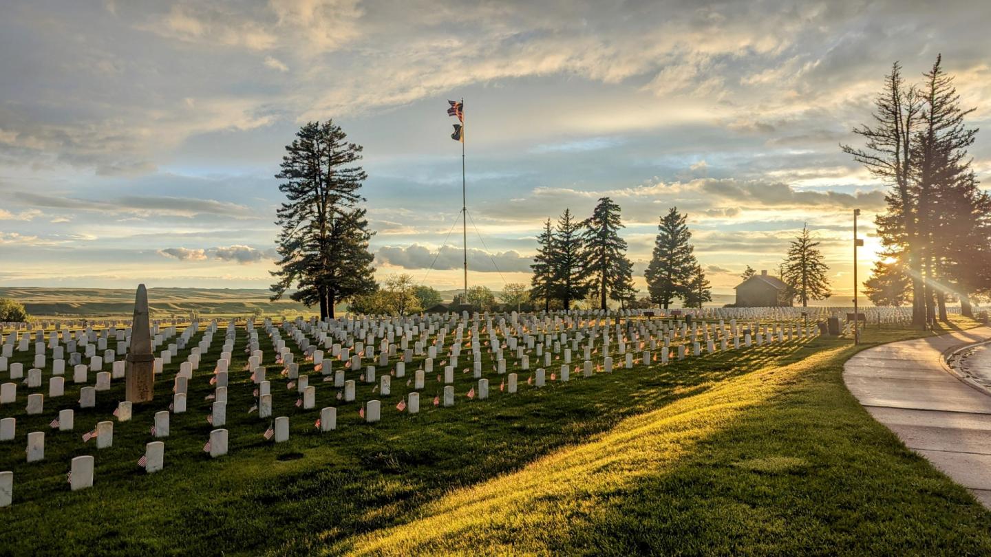 Sunset over a cemetery with rows of white headstones and a flagpole.