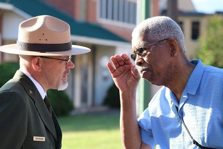 Tom Medema in uniform talks to a man in blue shirt outdoors.