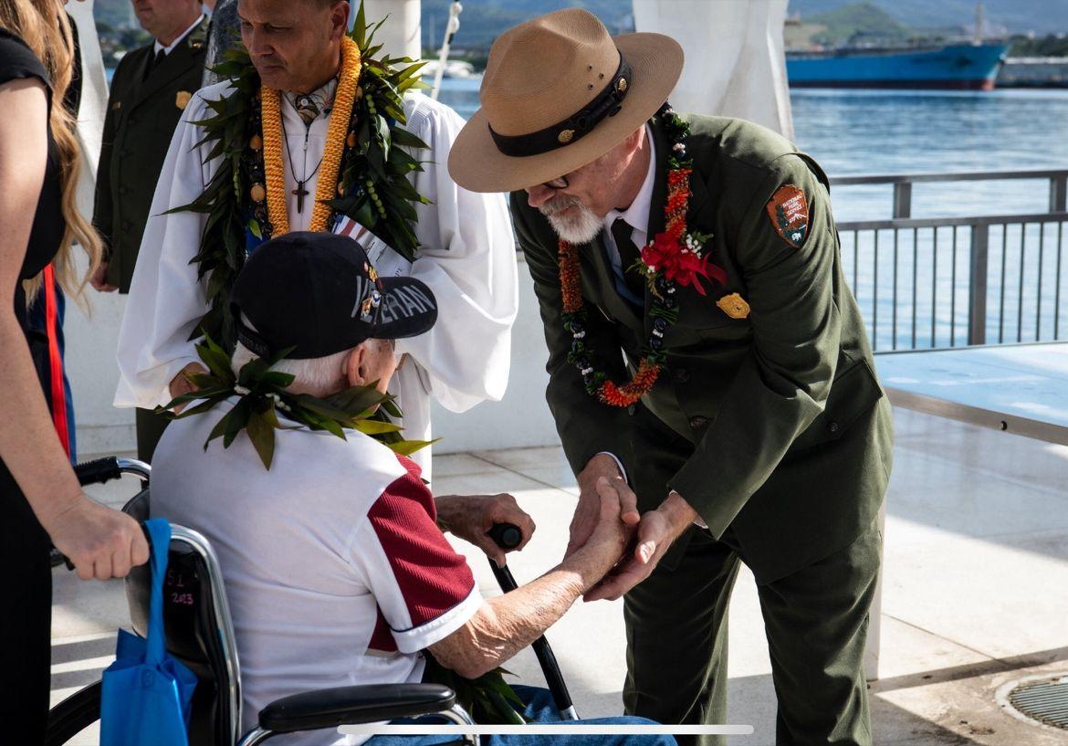 Park ranger greeting an elderly person in a wheelchair by the water.