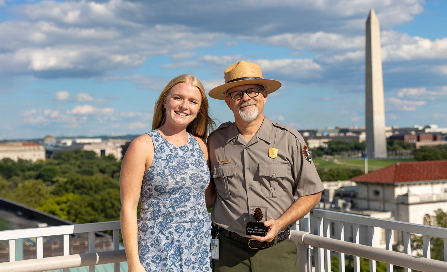 Tom Medema and another individual pose on a rooftop near the Washington Monument on a sunny day.