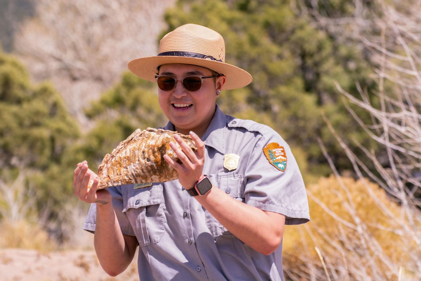 Park ranger in uniform holding a large shell outdoors.